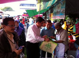 SIM Tze Tzin (berkemeja putih) menyampaikan beg kitar semula dan apron kepada salah seorang peniaga di Bazar Ramadhan Bayan Baru di sini barubaru ini.